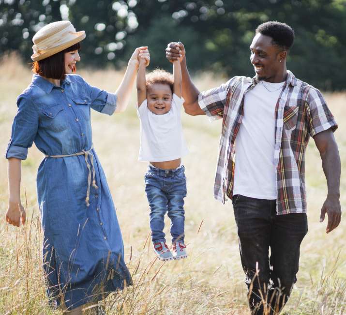 Cheerful african man and charming caucasian woman taking fun with little son during sunny say on nature.